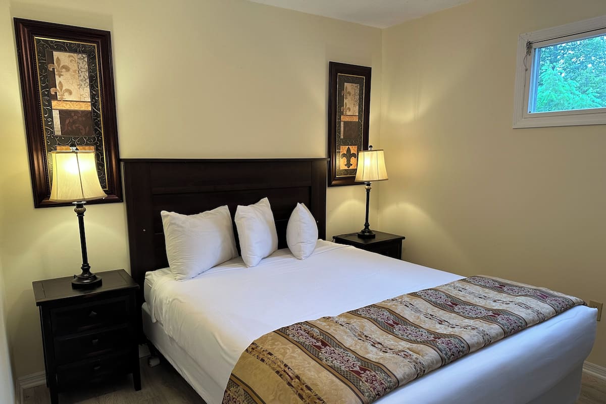 A neatly made bed with white linens, two bedside tables with lamps, and two framed pictures on the walls.