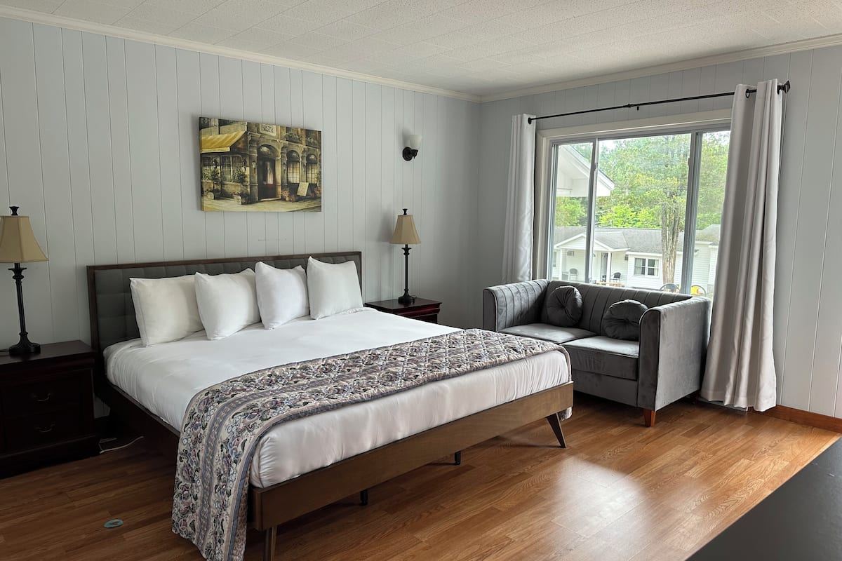 A neatly arranged bedroom with a bed, bedside tables, a sofa, and a large window.