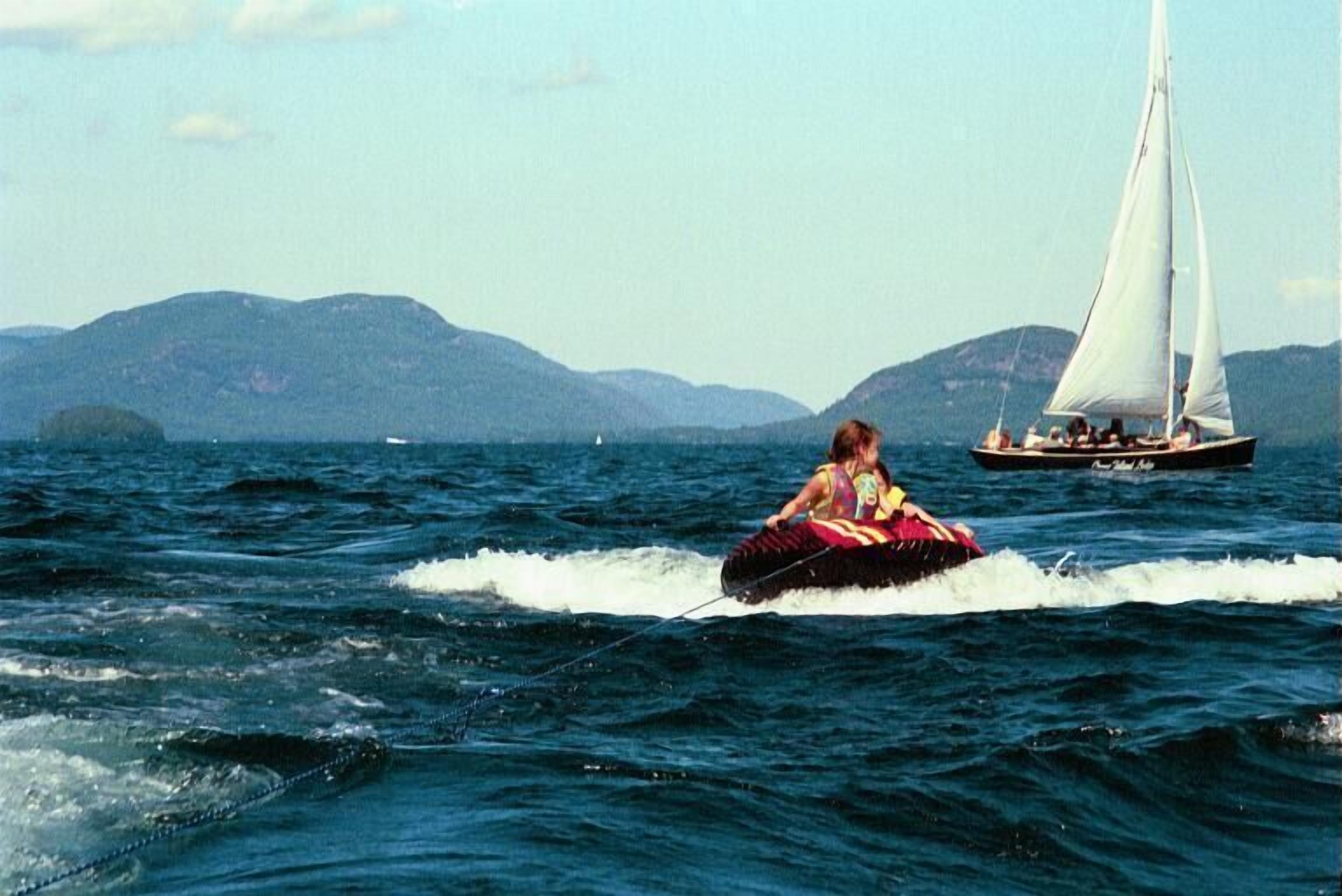 A person jet-skiing on a body of water with a sailboat in the background.