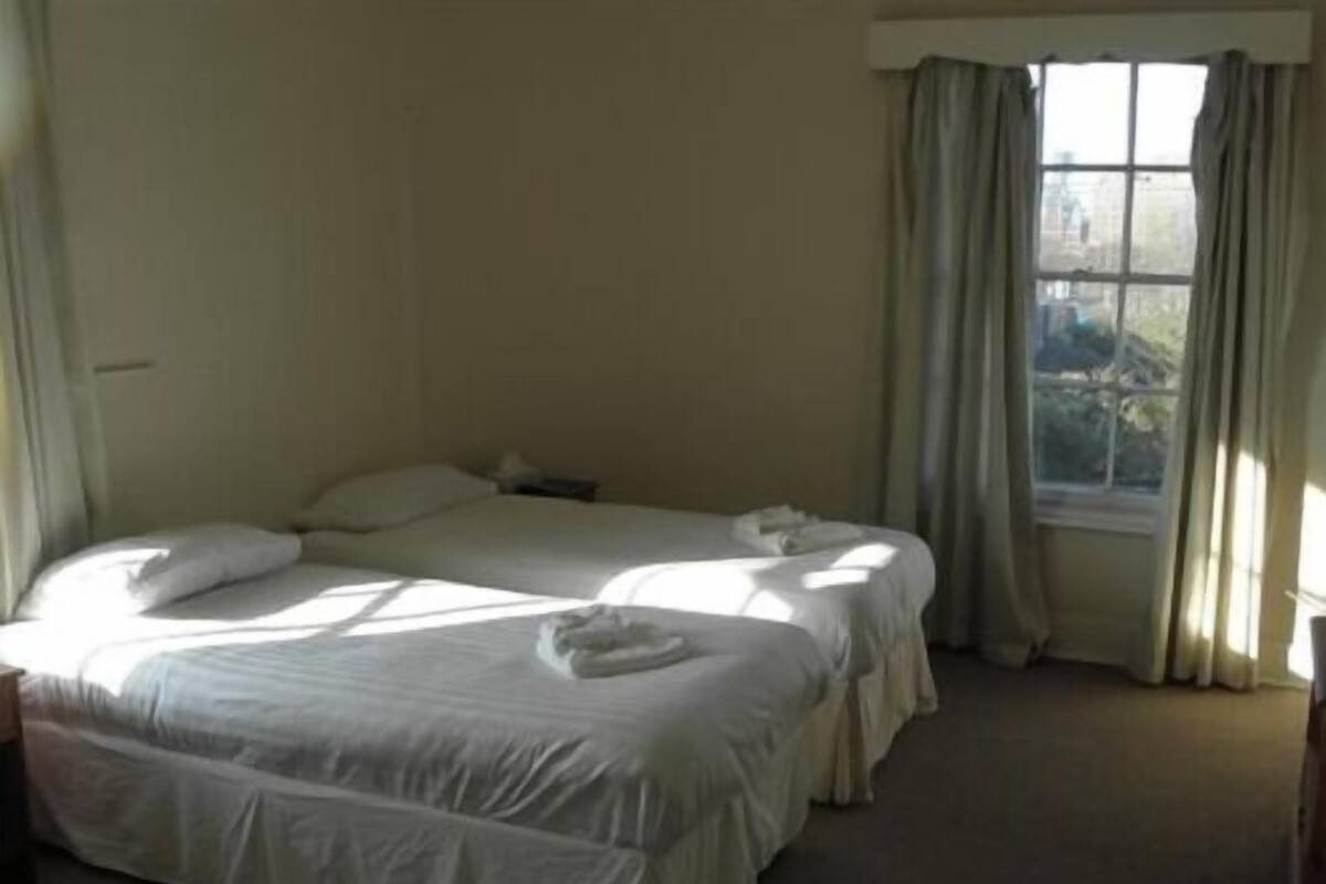 A hotel room with two beds, a window with curtains, and a carpeted floor.