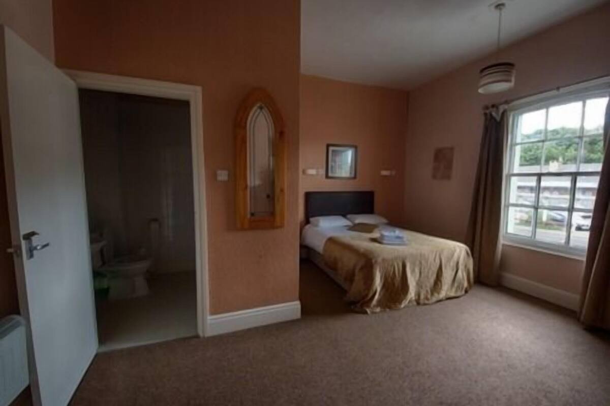 A bedroom with a bed, a window, and a door leading to a bathroom.
