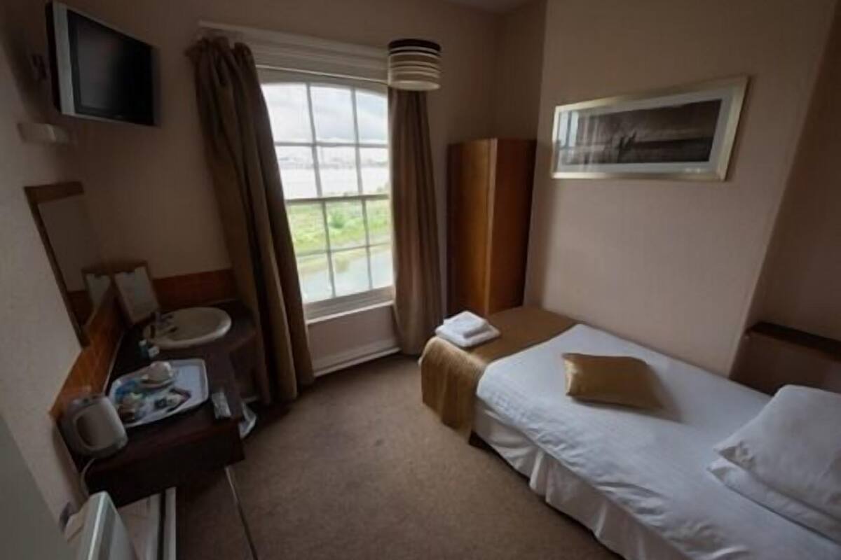 A hotel room with a bed, a bedside table, a TV, a window, and a bathroom.