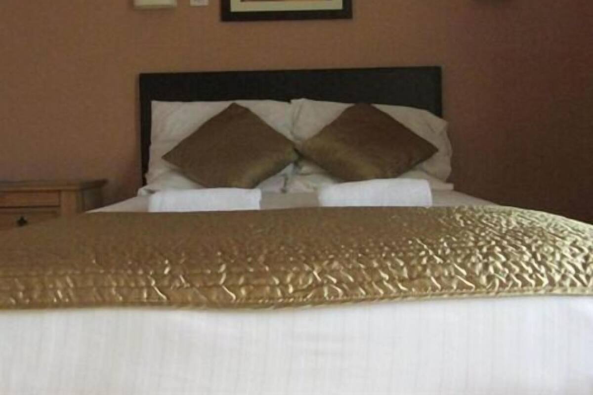 A neatly made bed with a gold-colored bedspread and two brown pillows.