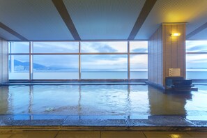 A large indoor swimming pool with a view of a body of water and mountains through large windows. - Biwako Hotel (Otsu)