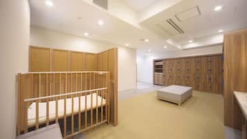 A room with a wooden crib, a small bed, a storage unit, and a locker area.
