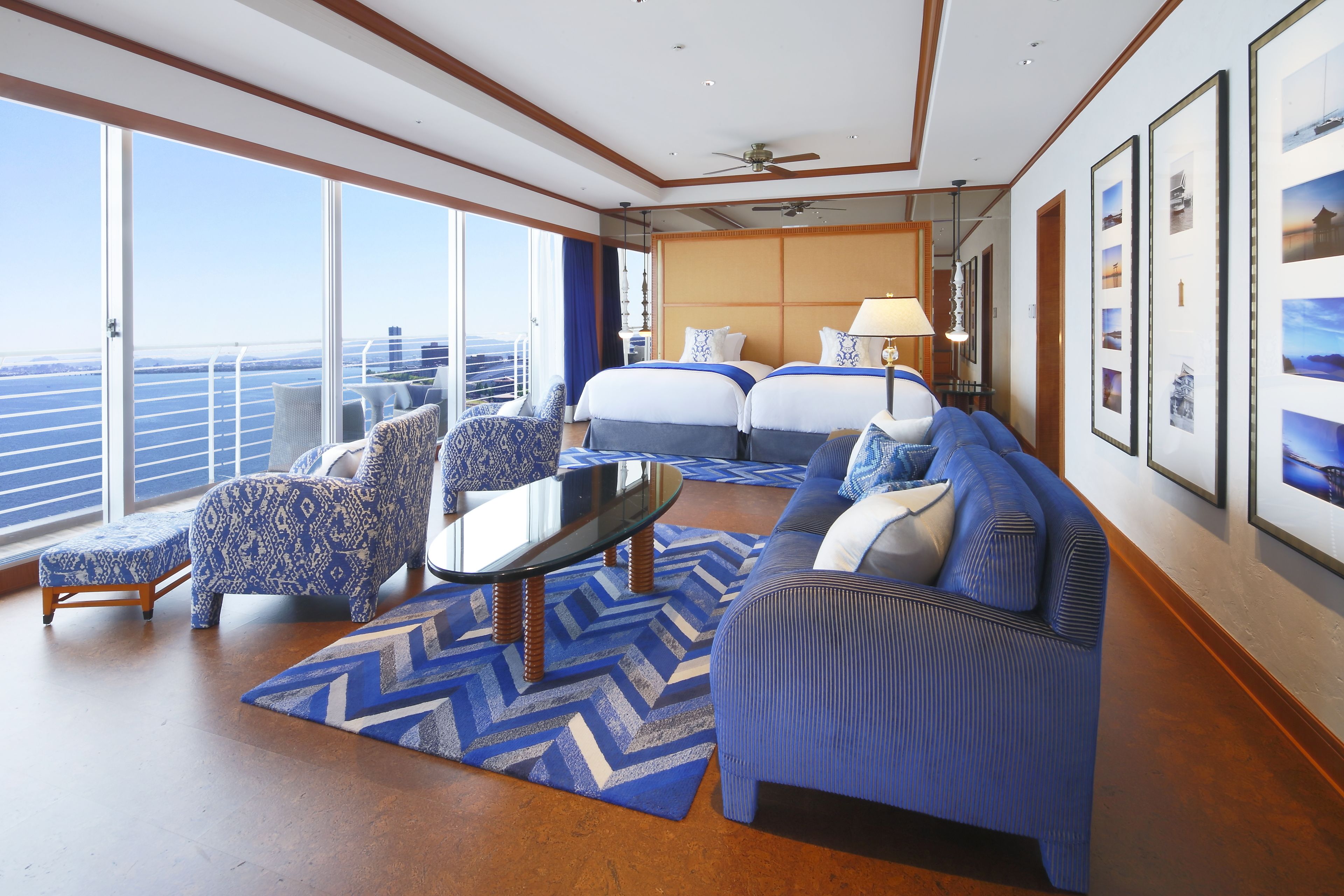 Amplia habitación con un gran ventanal que ofrece vistas al mar, una cama con cabecera, un sofá, una mesa de centro y un tapete estampado.
