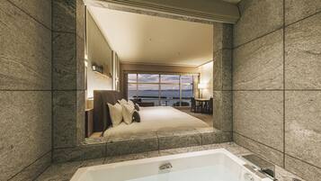 A modern hotel room with a large bed, a bathtub, and a view of the sea.