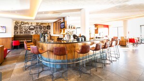 Zona de bar moderna con una barra curvada, varios taburetes, una pantalla de televisión y una variedad de botellas en estanterías.