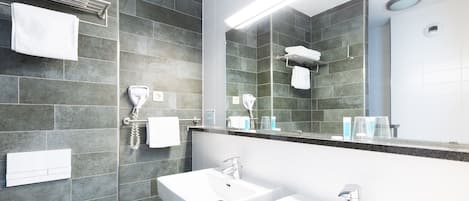 Un baño moderno con baldosas de piedra oscura, dos lavamanos, un espejo grande y secadores de pelo montados en la pared.