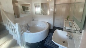 A bathroom with a large bathtub, a sink, and a mirror. There is a door and a staircase leading to another room. - The Old Court Hotel (Witney)