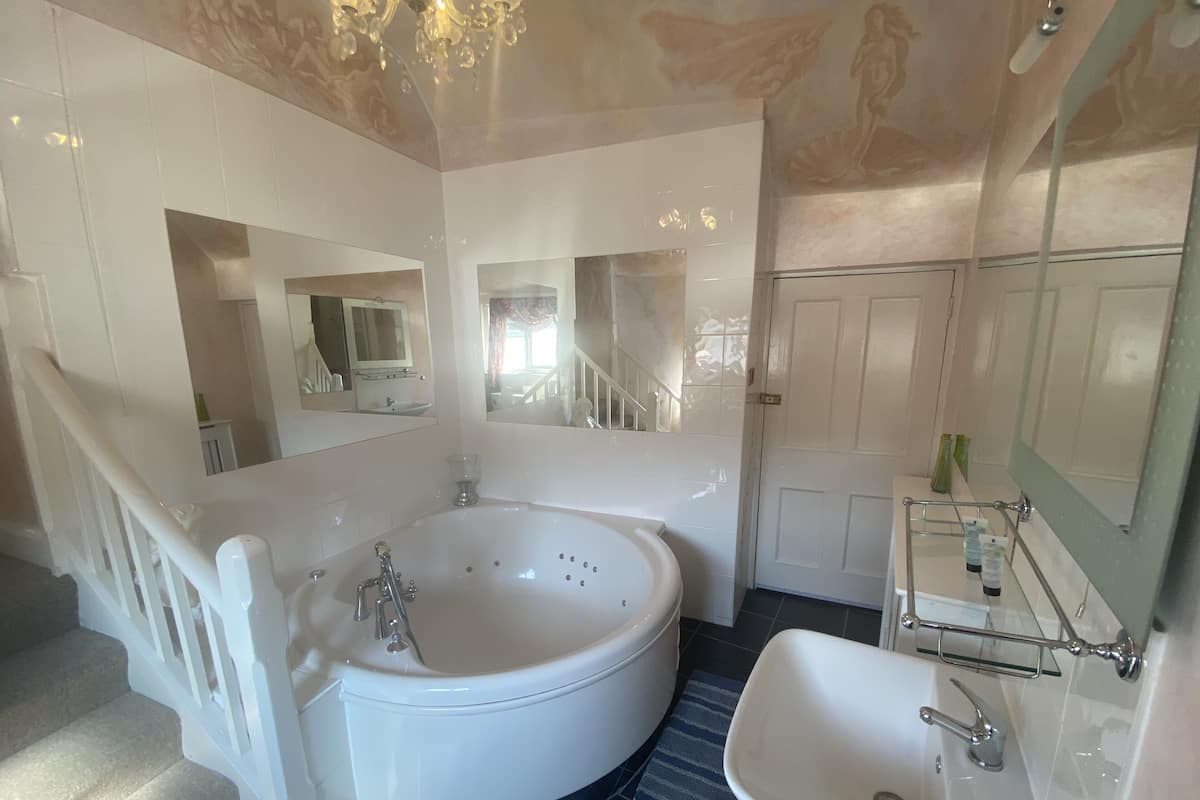 A bathroom with a large bathtub, a sink, and a mirror. There is a door and a staircase leading to another room.