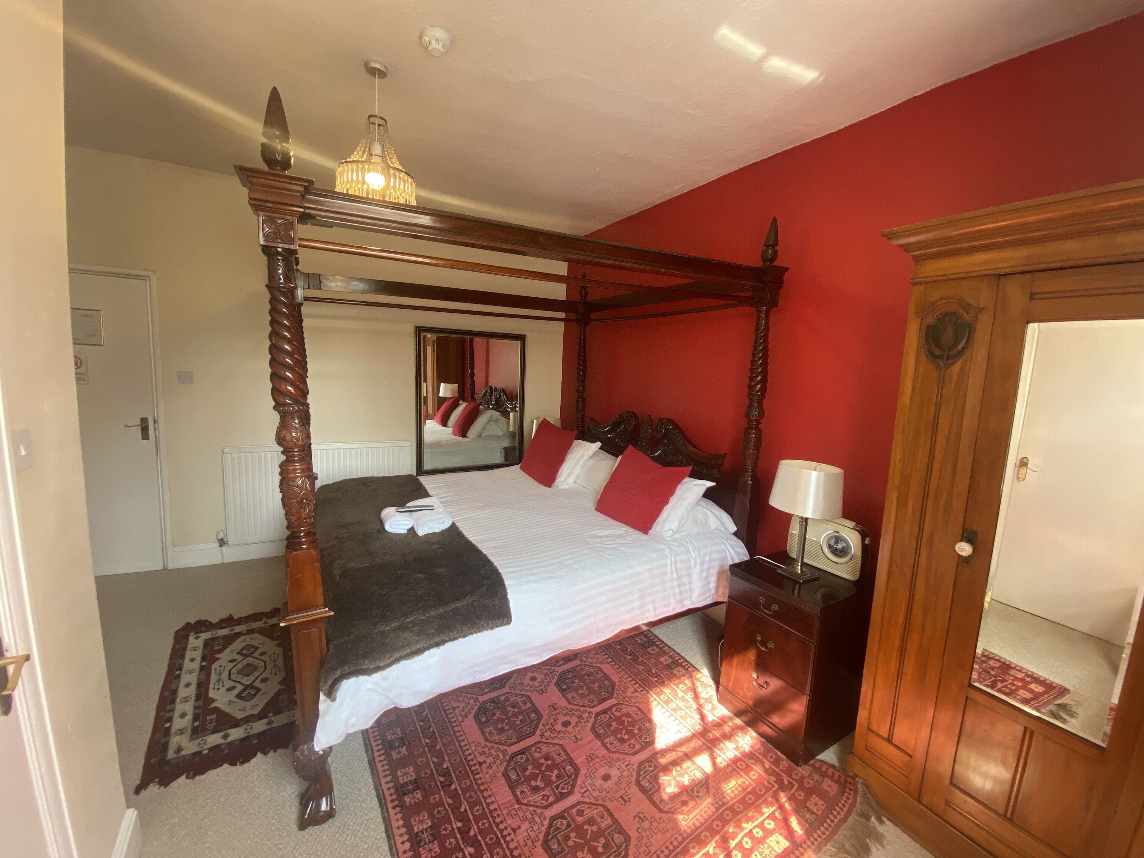 A four-poster bed with a mirror, a bedside table with a lamp, and a wooden wardrobe.