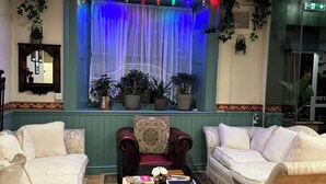 A cozy living room with a patterned rug, two white sofas, a dark wooden coffee table with books, and a window with blue lighting. - The Old Court Hotel (Witney)