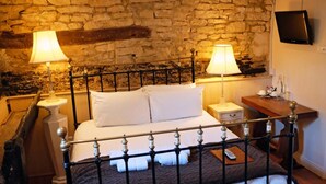 A bed with white linens, two bedside lamps, a wooden nightstand, a remote control, and a stone wall. - The Old Court Hotel (Witney)