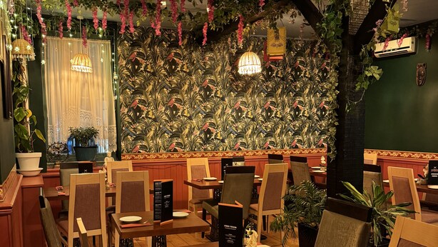 A restaurant with wooden tables and chairs, hanging plants, and decorative lights. - The Old Court Hotel (Witney)