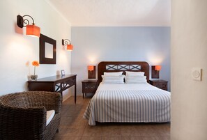 A neatly arranged hotel room with a large bed, two bedside tables, a wicker chair, and wall-mounted lamps. - Hotel Rural Monte Da Leziria (Santiago do Cacém)