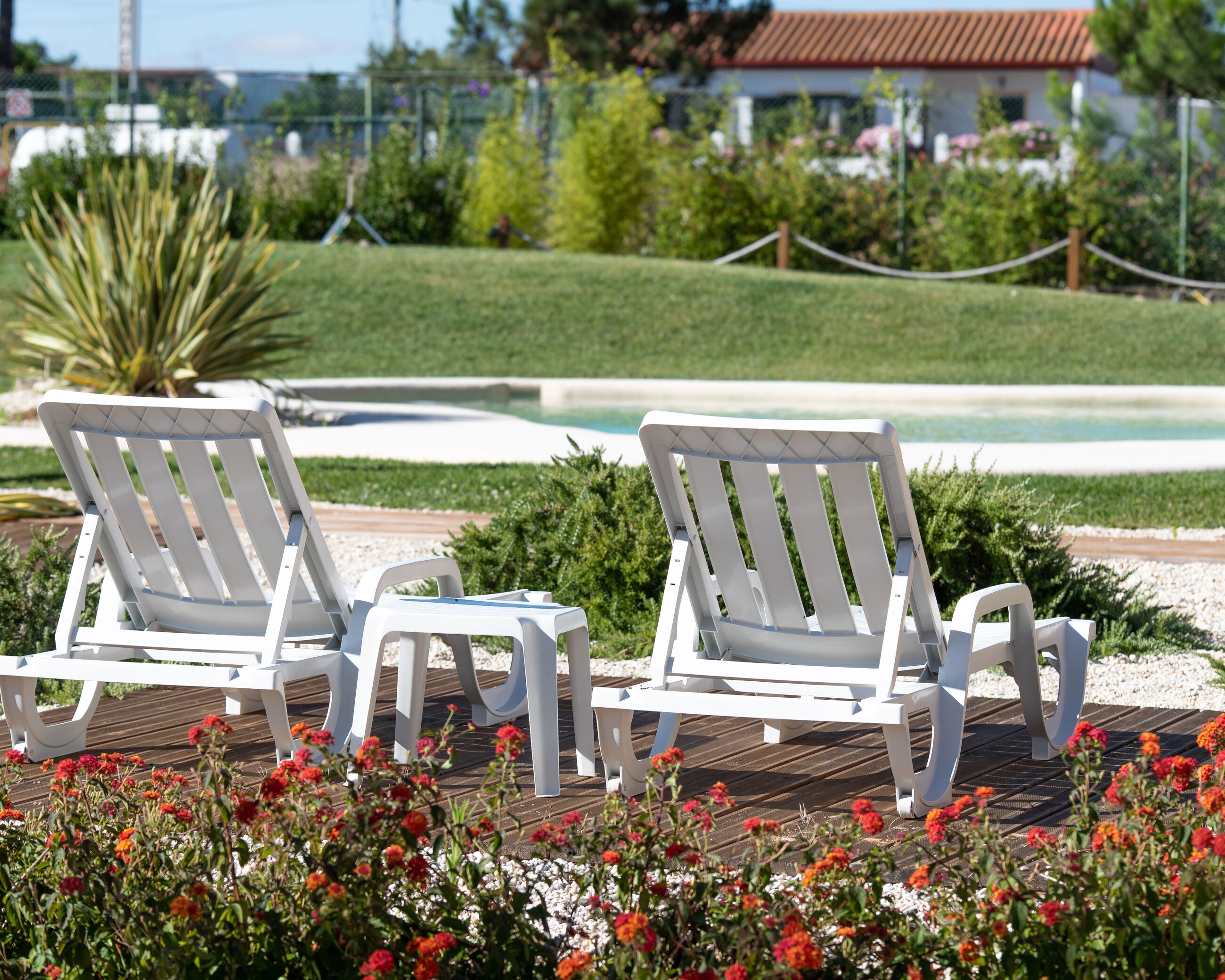 Two white lounge chairs on a wooden deck with a pool in the background.