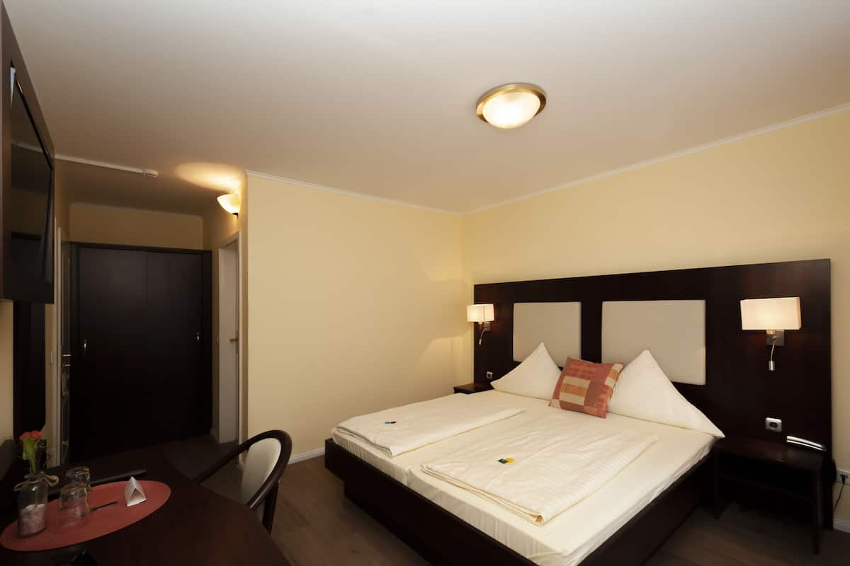A hotel room with a large bed, two bedside tables with lamps, a small table with a vase and candles, and a chair.