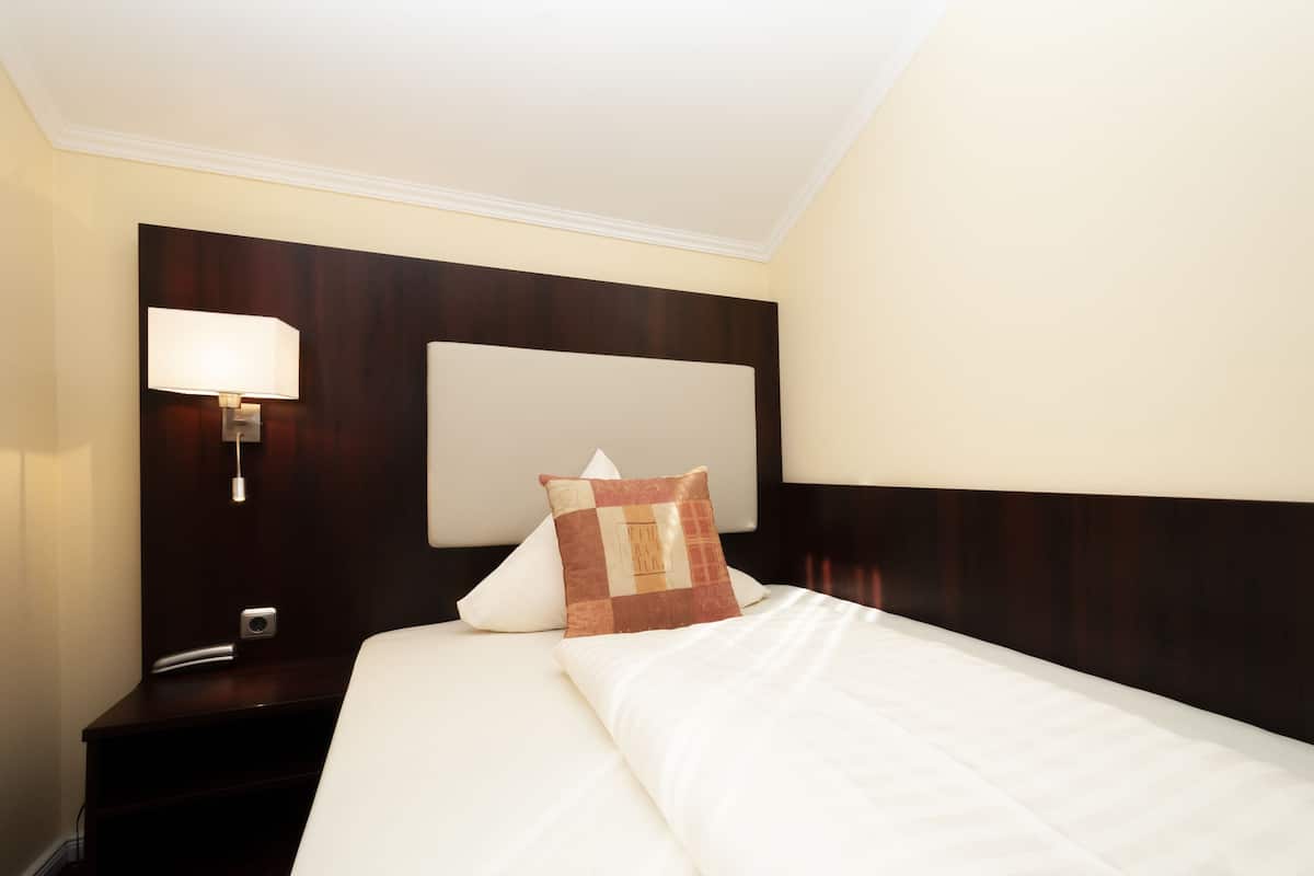 A hotel room with a neatly made bed, a bedside lamp, and a nightstand with a phone.