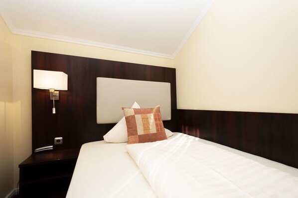 A hotel room with a neatly made bed, a bedside lamp, and a nightstand with a phone. - Hotel Grüne Tanne (Hamburg)