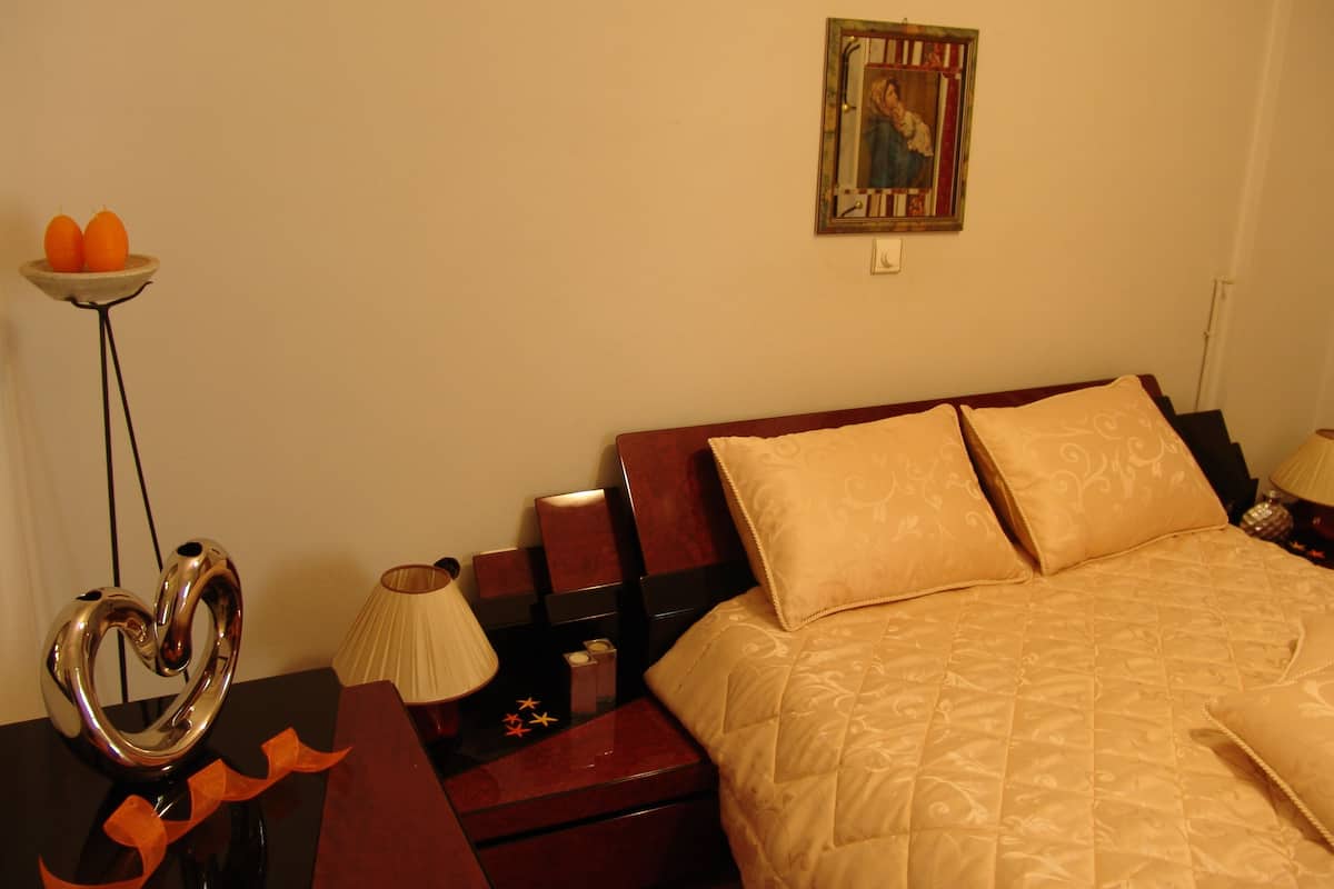 Ein Hotelzimmer mit Bett, Nachttisch, Lampe, einem dekorativen herzförmigen Gegenstand und einem gerahmten Bild an der Wand.