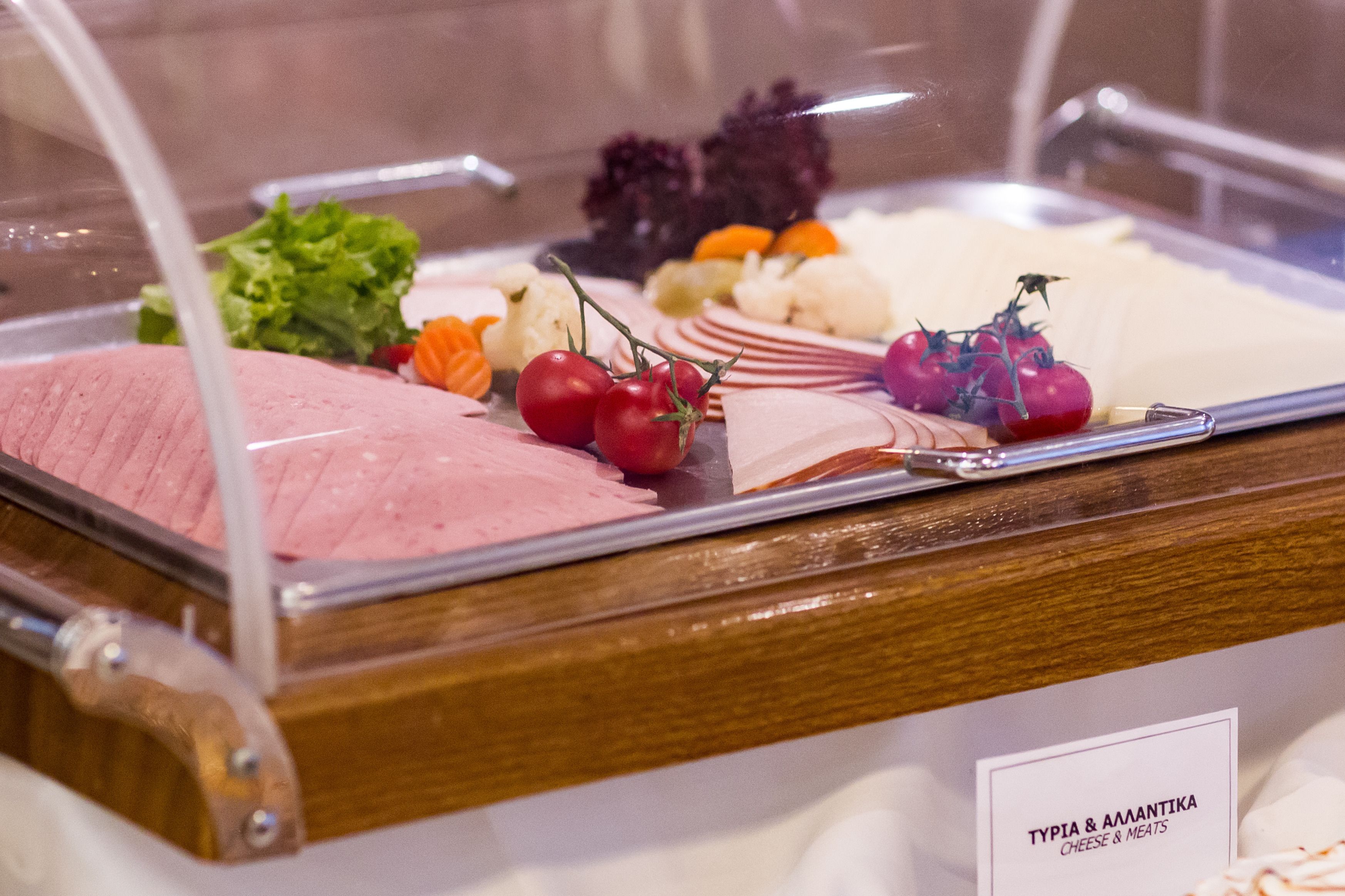 A food display with various cheeses and meats, including tomatoes and lettuce.