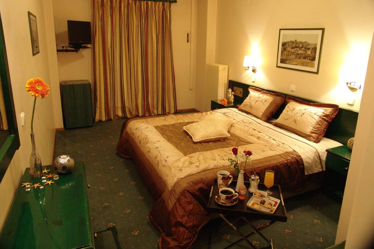 Ein Hotelzimmer mit einem Bett, einem Nachttisch mit Frühstücksgegenständen und einer Vase mit einer Blume sowie einem Bild an der Wand.