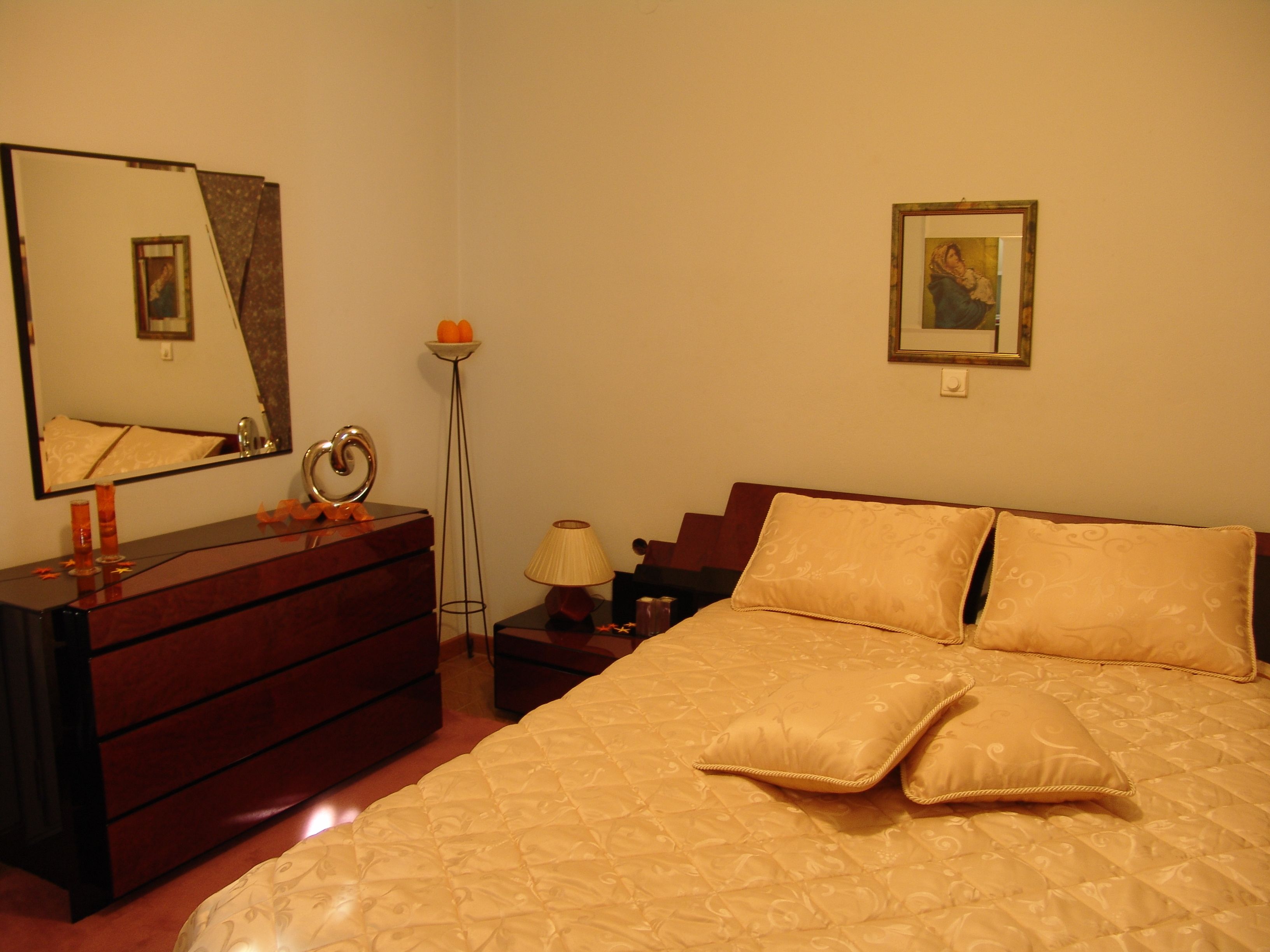 A bedroom with a bed, dresser, mirror, lamp, and a framed picture on the wall.