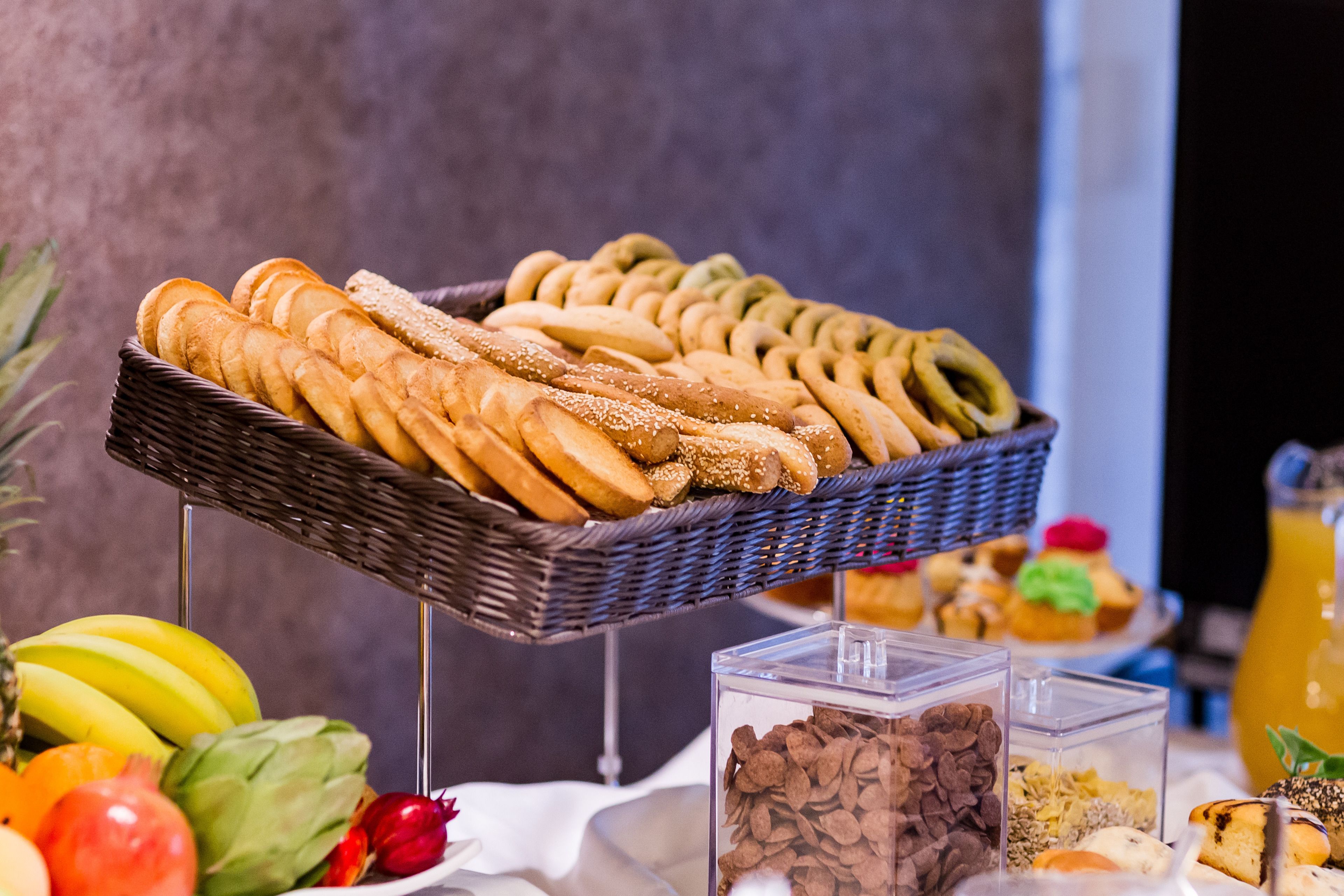 Un buffet con diversi tipi di pane, frutta e un distributore di bevande.