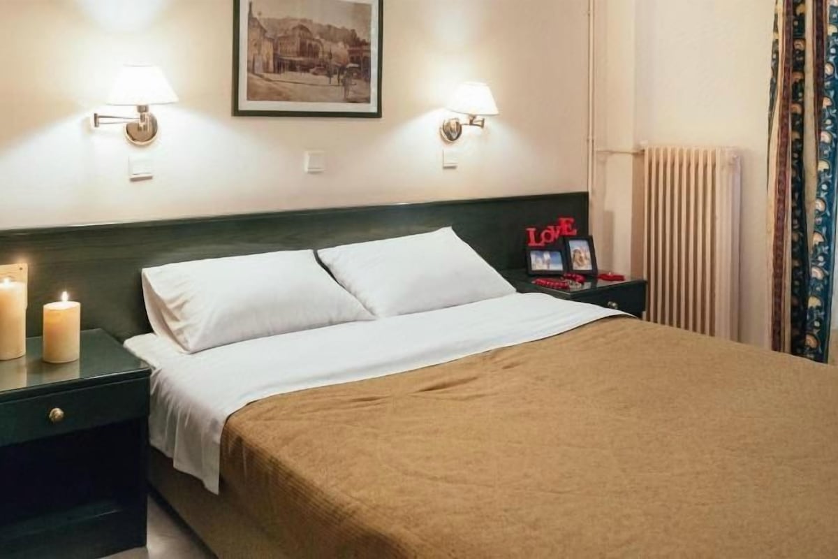 Una habitación de hotel con una cama, dos lámparas de noche, una mesita de noche, un marco de fotos y un objeto decorativo sobre la mesita.