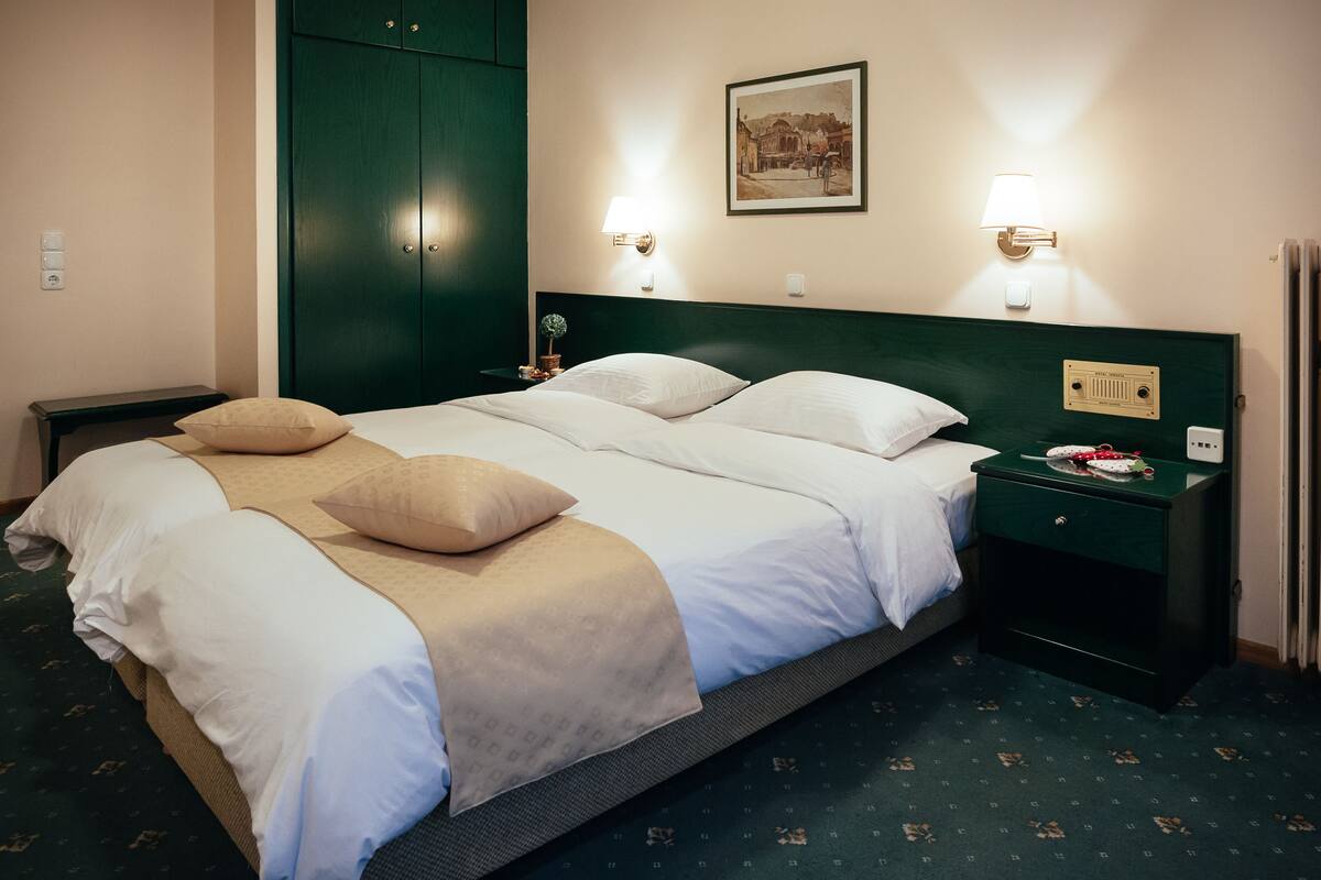 Ein Hotelzimmer mit einem großen Bett, zwei Nachttischen, einem grünen Kopfteil und einem gerahmten Bild an der Wand.