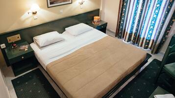 A hotel room with a bed, nightstands, a lamp, and a window with curtains.