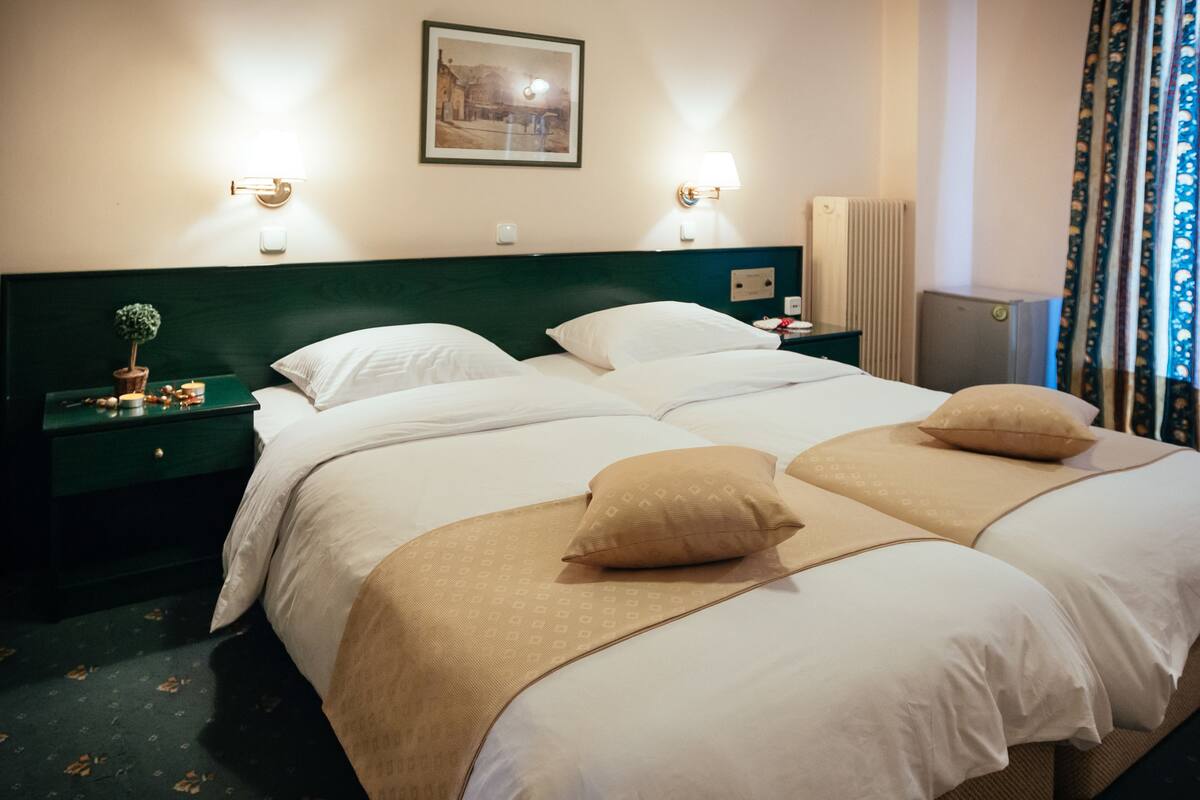 Ein Hotelzimmer mit einem großen Bett, zwei Nachttischen, einer Ablage, einer Wandlampe, einem gerahmten Bild und einem Heizkörper.