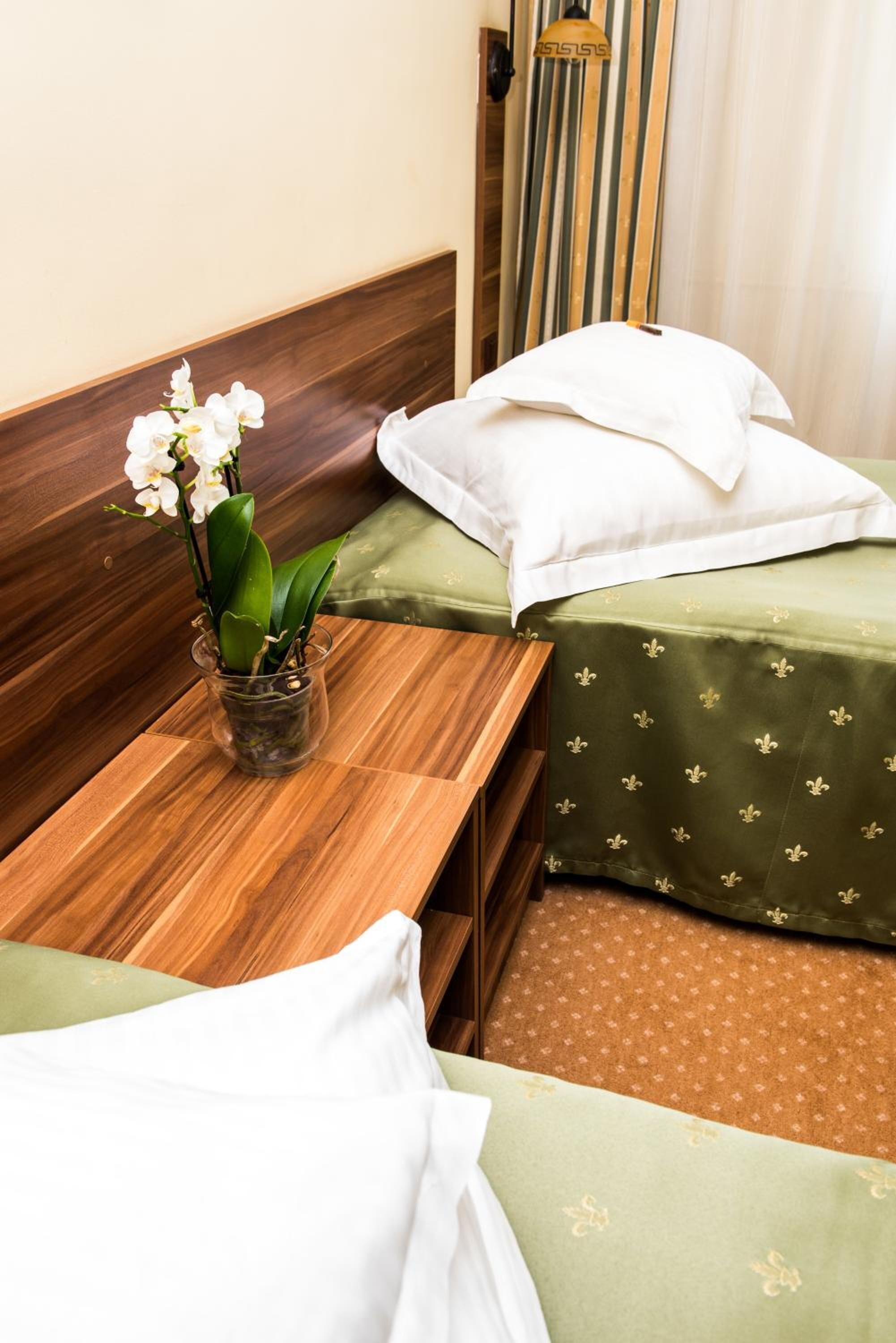 A hotel room with a wooden headboard, a small table with a vase of white orchids, a bed with green bedding, and a striped curtain.