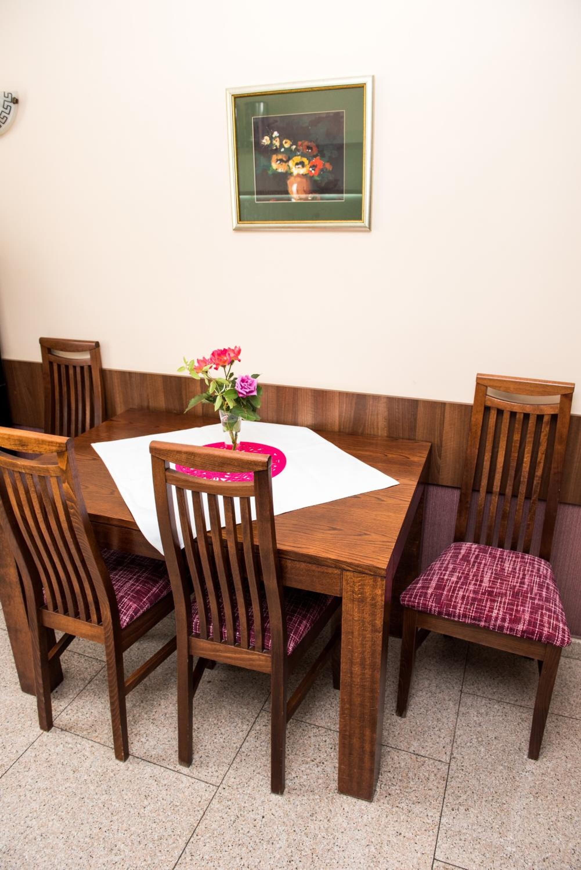 Un comedor con una mesa de madera y cuatro sillas, una con cojín a cuadros. Sobre la mesa, hay un cuadro enmarcado en la pared.