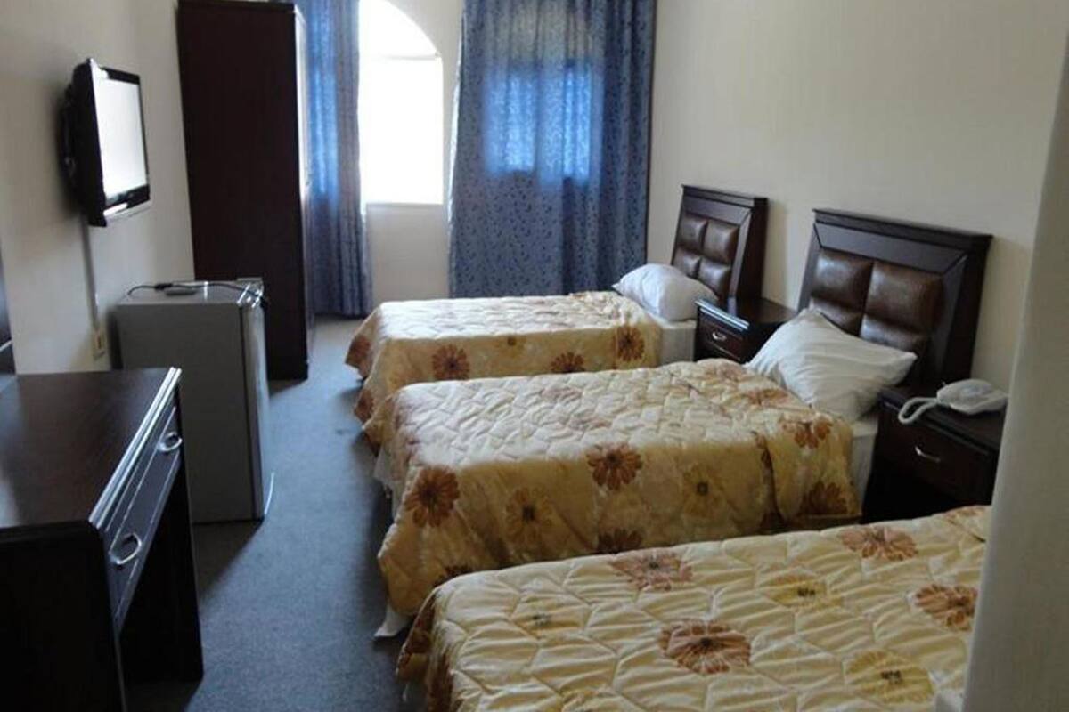 A hotel room with three beds, a desk, a dresser, and a television.