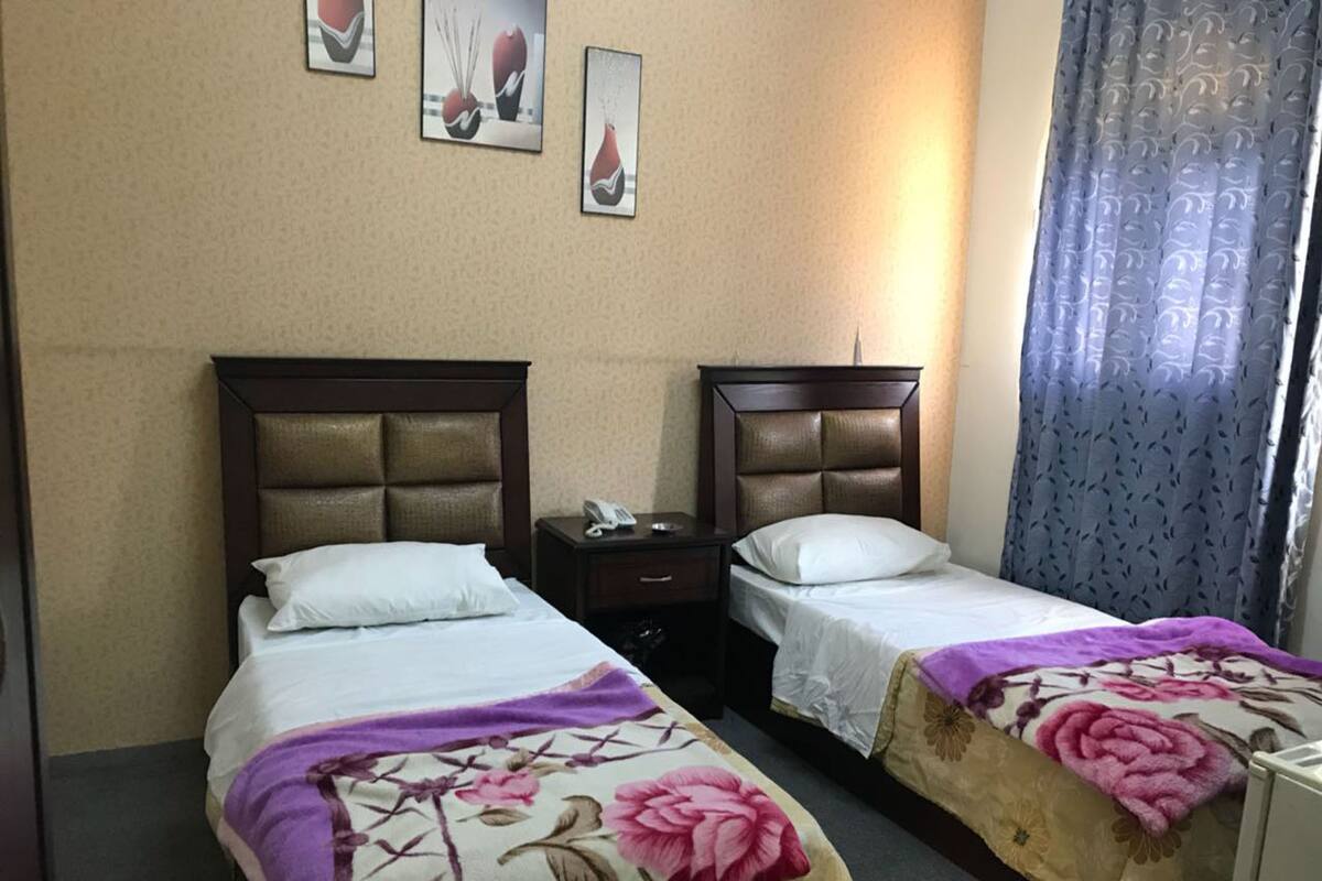 A hotel room with two beds, each with a headboard, a bedside table with a phone, and a curtain.