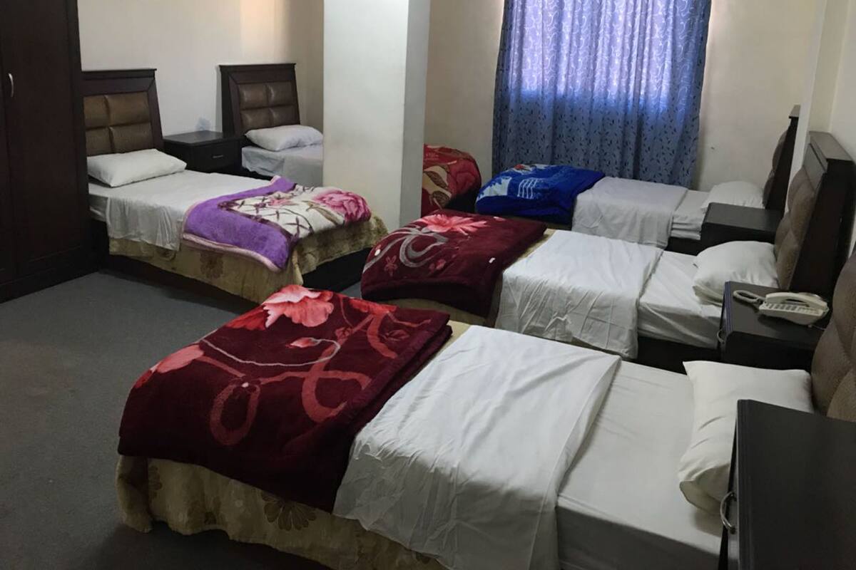 A hotel room with three single beds, each with a different colored blanket, a desk with a telephone, and a window with curtains.