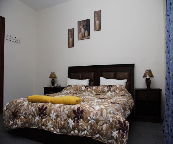 Un dormitorio con colcha estampada, dos lámparas de noche, cabecero de madera y tres cuadros en la pared.
