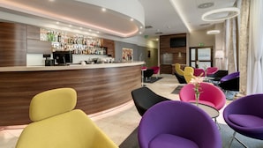 A modern bar area with a curved counter, various seating options including colorful chairs, and a well-stocked bar. - Golden Tulip Krakow City Center (Kraków)