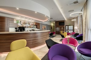 Eine moderne Bar mit gebogener Theke, verschiedenen Sitzgelegenheiten, darunter farbenfrohe Stühle, und einer gut sortierten Bar.