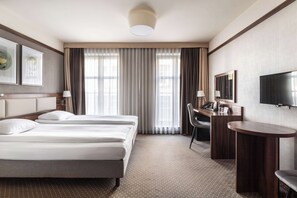 A hotel room with two beds, a desk, a chair, a television, and a large window with curtains. - Golden Tulip Krakow City Center (Kraków)