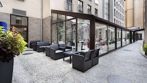 An outdoor seating area with wicker furniture and a cobblestone floor. - Golden Tulip Krakow City Center (Kraków)