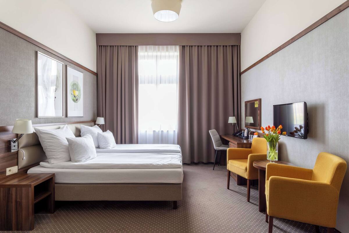 Habitación de hotel con cama, dos sillas, escritorio, televisor y obras de arte en las paredes.