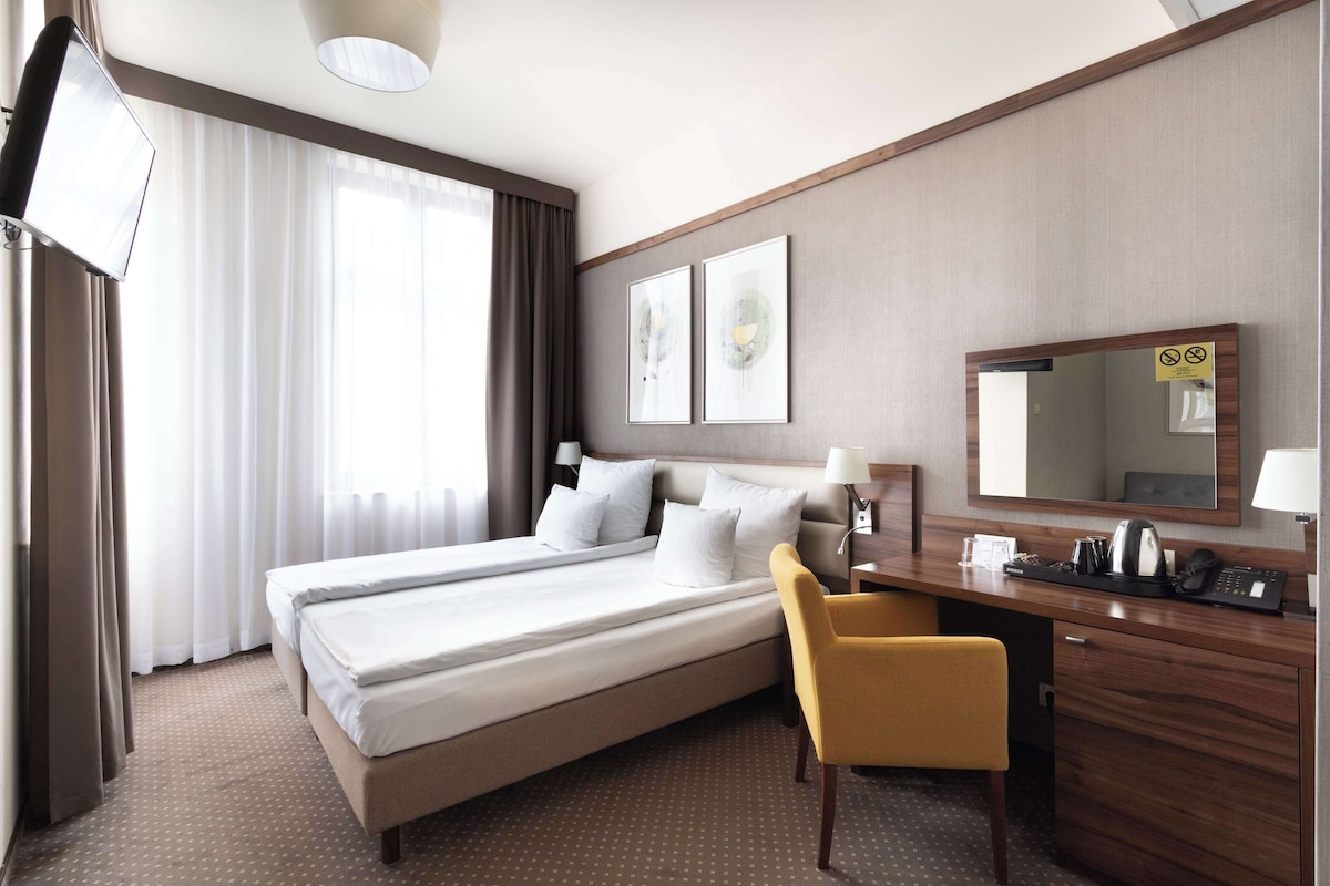 Une chambre d’hôtel équipée d’un lit, d’un bureau, d’une chaise, d’une télévision et d’une grande fenêtre avec des rideaux.