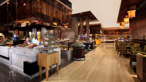 Un hall d’hôtel moderne doté d’un espace central où sont présentés des plats, de coins salon et d’une grande façade vitrée.
