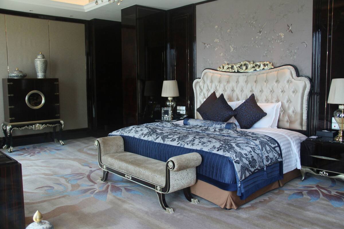 A bedroom with a large bed, a chaise lounge, a dresser, and a mirror.