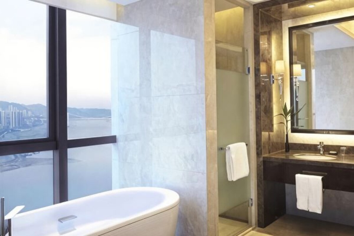 Un baño moderno con una bañera grande, cabina de ducha de vidrio y vistas a la ciudad a través de un ventanal.