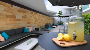 Un espacio exterior con mobiliario moderno, que incluye una pared de piedra, una mesa negra y un dispensador de bebidas de vidrio.