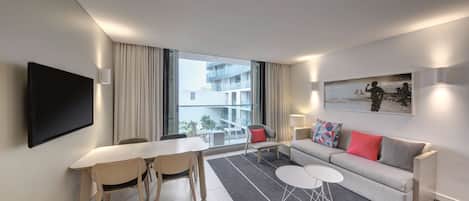 Ein modernes Hotelzimmer mit Essbereich, einer Couch und einem großen Fenster mit Blick auf das Gebäude.